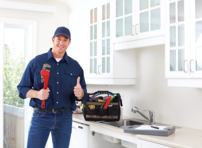 Smiling plumber in kitchen giving a thumb's up. Their tool bag sits on the bench