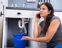 Worried Woman Calling Plumber While Collecting Water Leaking From Sink